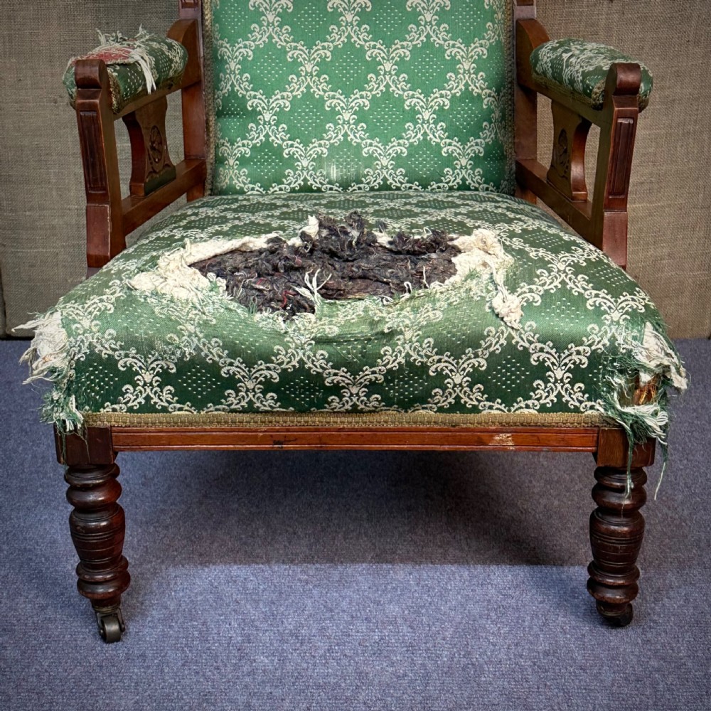 A Victorian carved mahogany armchair featuring a floral cresting rail, turned front legs on castors, and worn green patterned upholstery. View VI