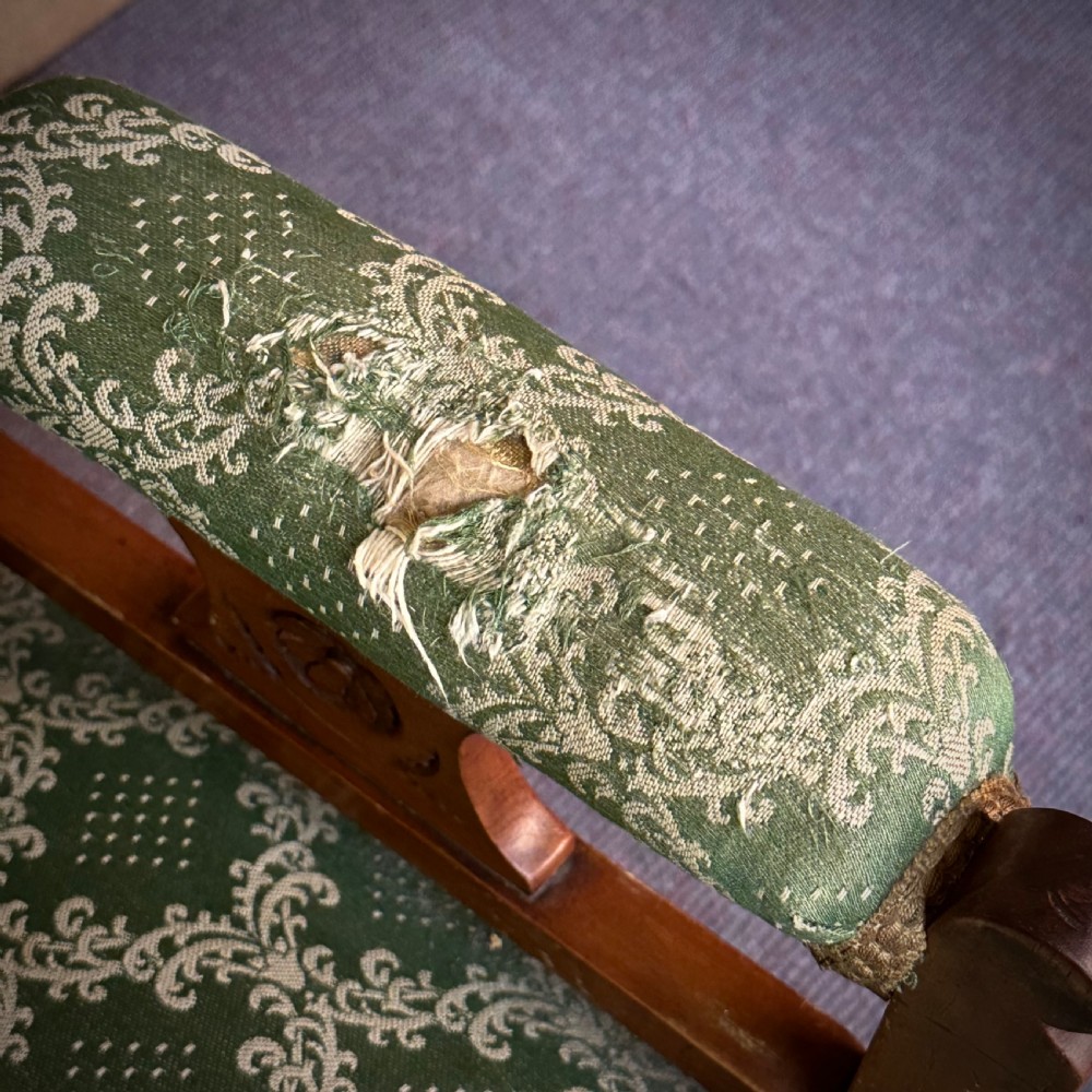 A Victorian carved mahogany armchair featuring a floral cresting rail, turned front legs on castors, and worn green patterned upholstery. View VIII