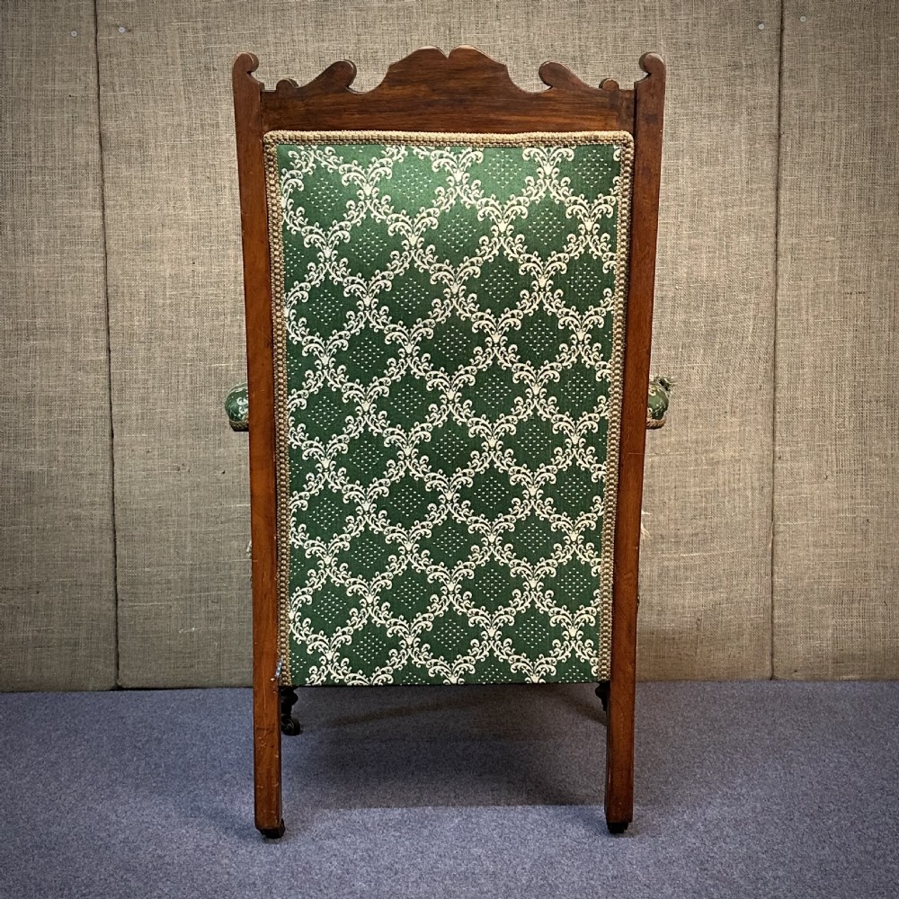 A Victorian carved mahogany armchair featuring a floral cresting rail, turned front legs on castors, and worn green patterned upholstery. View IX