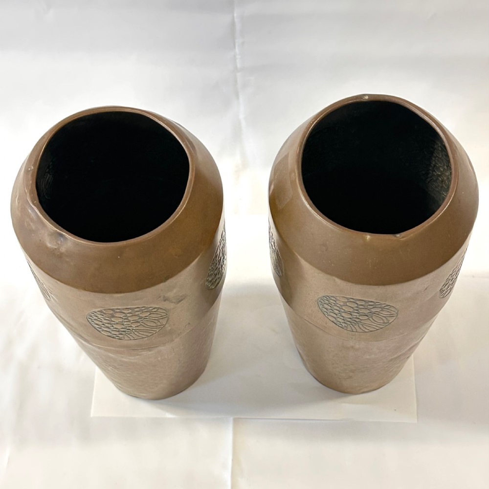 A pair of cylindrical brass vases featuring hand-hammered lower bodies and circular embossed floral medallions around the upper rim. View II