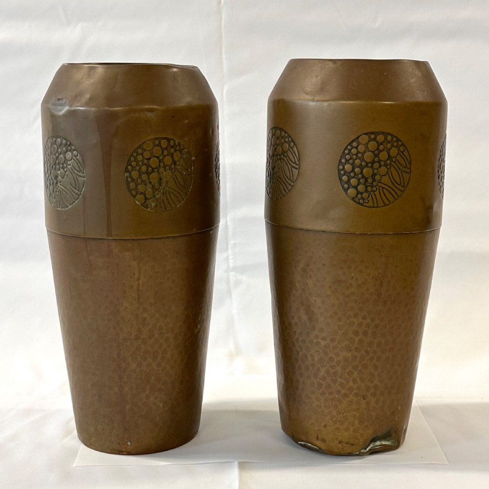 A pair of cylindrical brass vases featuring hand-hammered lower bodies and circular embossed floral medallions around the upper rim. View III