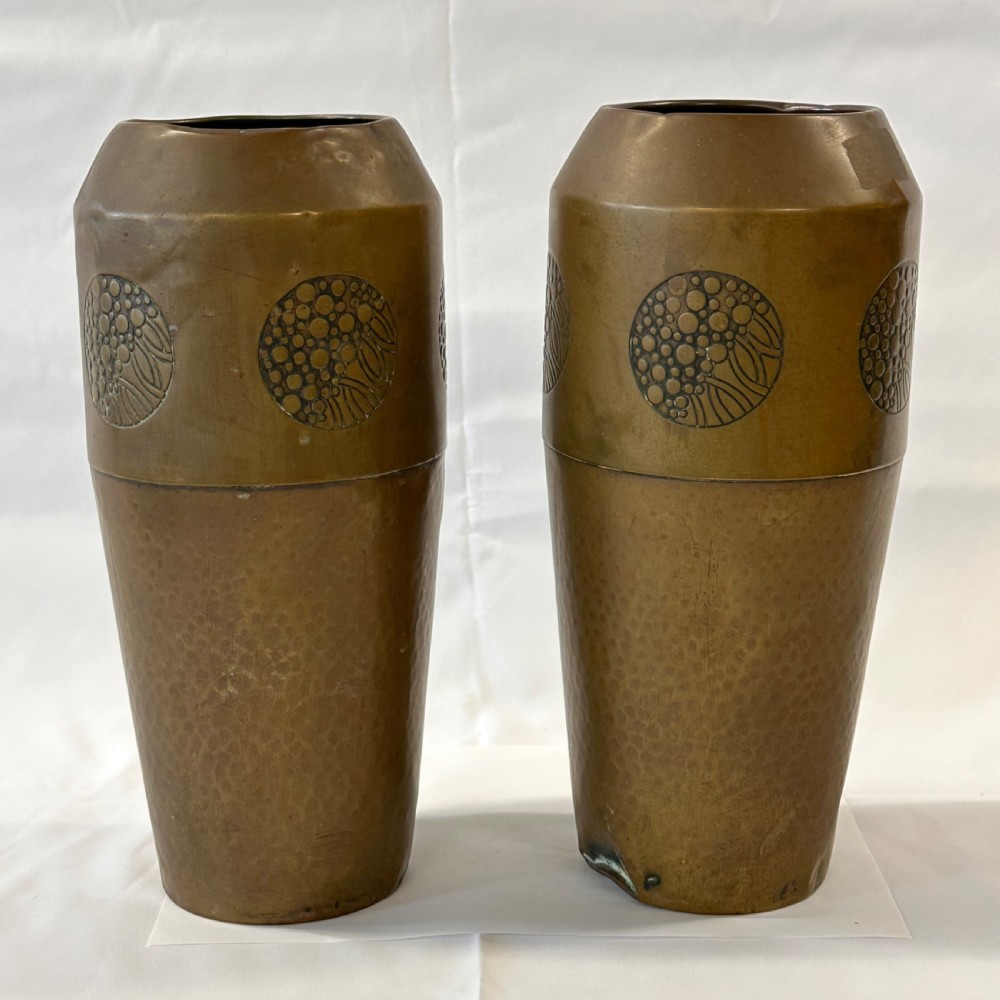 A pair of cylindrical brass vases featuring hand-hammered lower bodies and circular embossed floral medallions around the upper rim. View IV