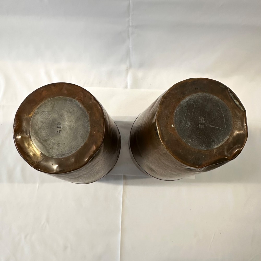A pair of cylindrical brass vases featuring hand-hammered lower bodies and circular embossed floral medallions around the upper rim. View VI
