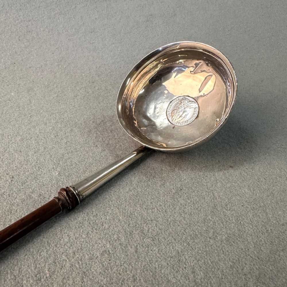 An 18th-century Georgian silver toddy ladle featuring an inset silver coin at the base of the bowl attached to a dark turned handle.