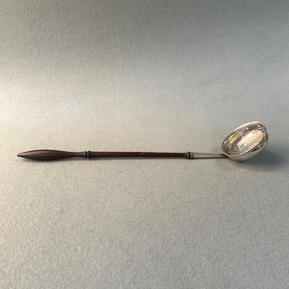 An 18th-century Georgian silver toddy ladle featuring an inset silver coin at the base of the bowl attached to a dark turned handle. View II