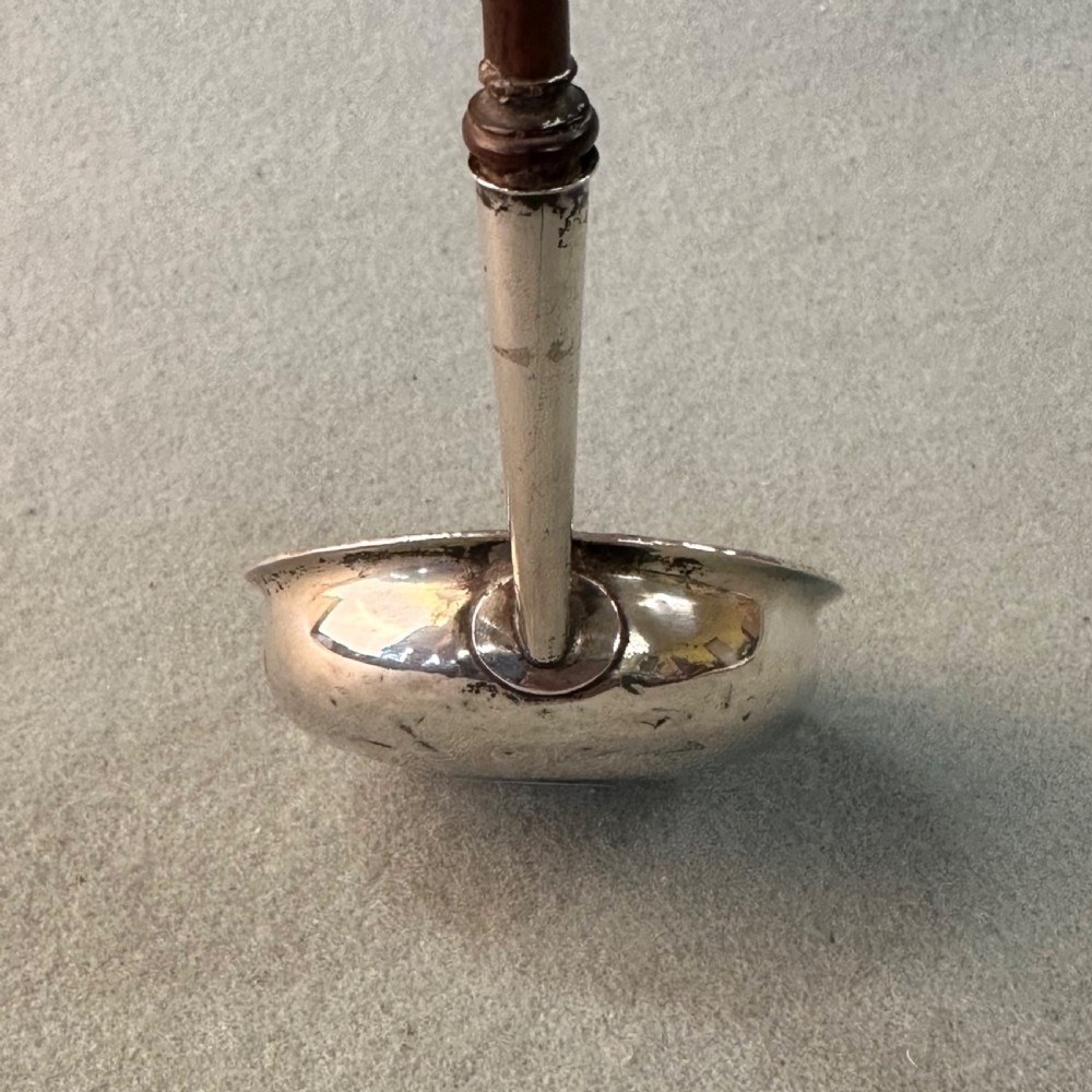 An 18th-century Georgian silver toddy ladle featuring an inset silver coin at the base of the bowl attached to a dark turned handle. View X