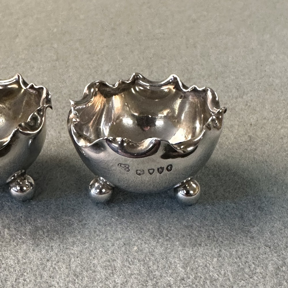 A pair of Victorian sterling silver open salt cellars featuring crimped rims, stamped hallmarks, and raised on three ball feet. View III