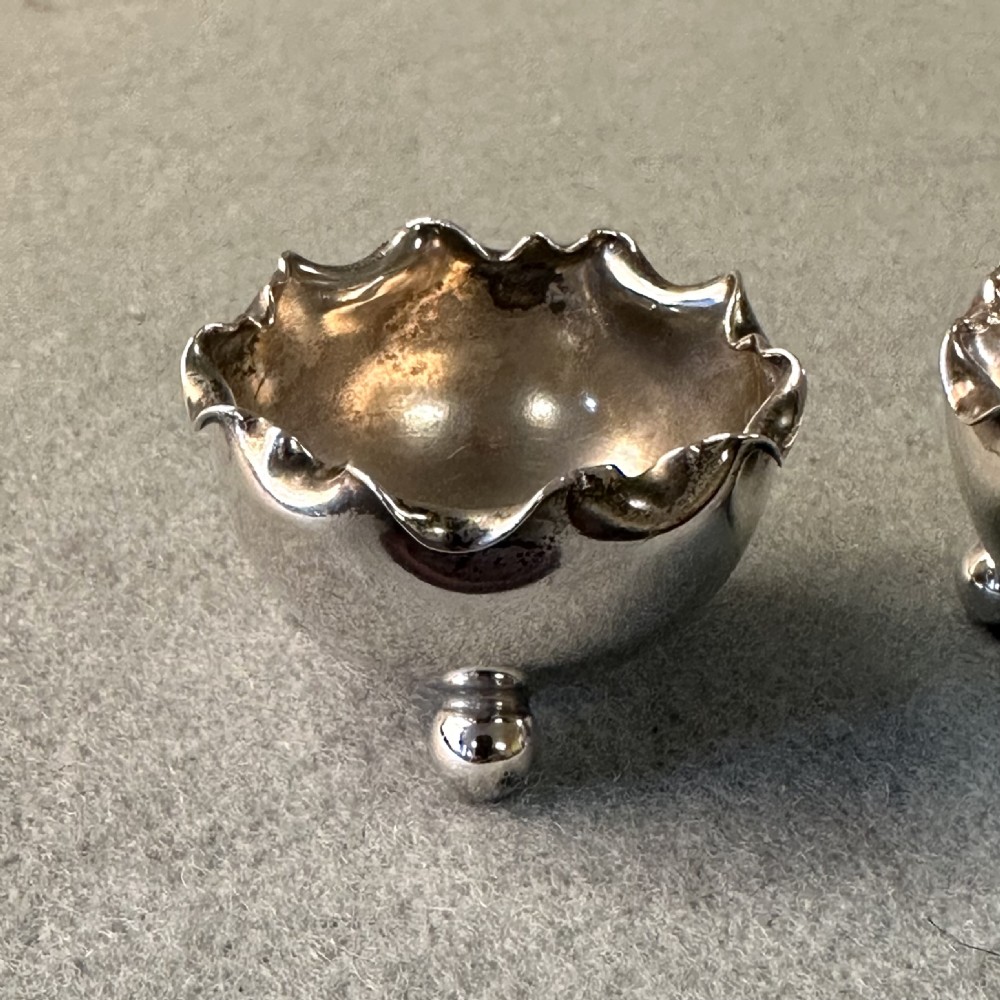 A pair of Victorian sterling silver open salt cellars featuring crimped rims, stamped hallmarks, and raised on three ball feet. View IV