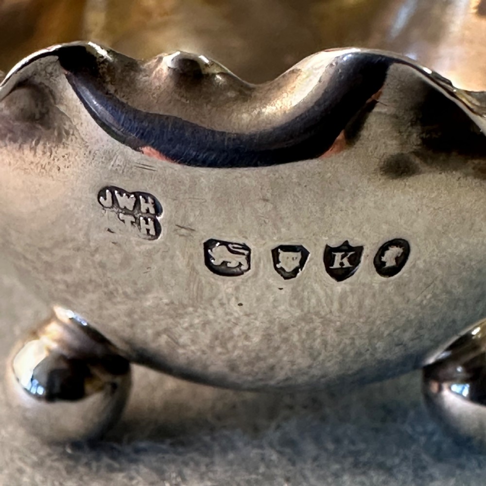 A pair of Victorian sterling silver open salt cellars featuring crimped rims, stamped hallmarks, and raised on three ball feet. View VI