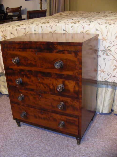 fig 3. A miniature Regency mahogany chest of four drawers featuring flame mahogany veneer drawer fronts, turned wooden knobs, brass keyholes, and short turned feet.