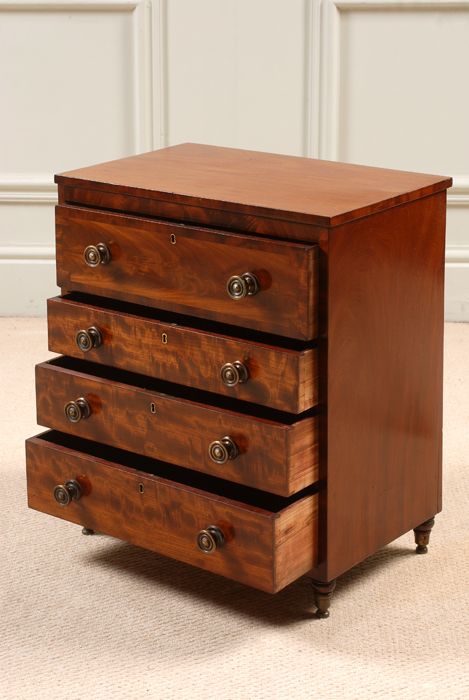 fig 1. A miniature Regency mahogany chest of four drawers featuring flame mahogany veneer drawer fronts, turned wooden knobs, brass keyholes, and short turned feet.