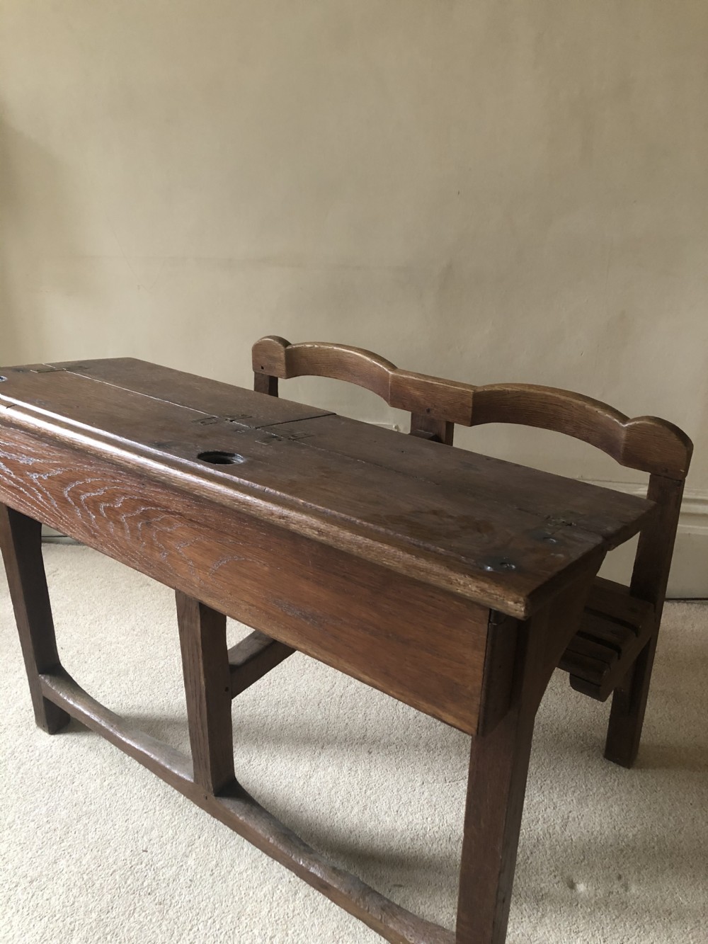 An antique medium brown wooden double school desk featuring an integrated bench seat, inkwell cutout, and double-arched backrest.