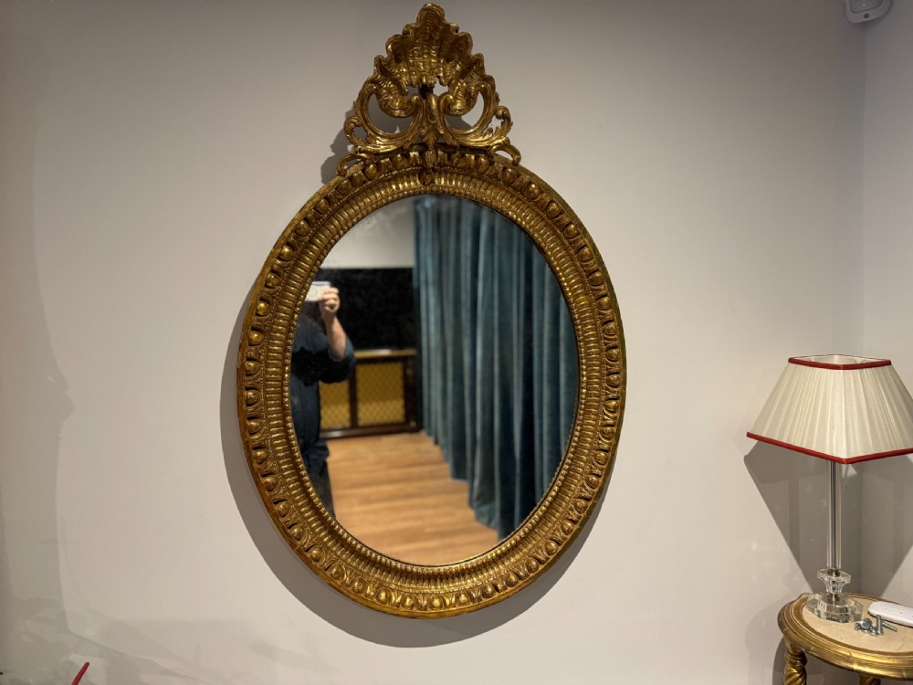 A George III period oval wall mirror featuring a carved giltwood frame with cresting detail and molded inner borders.