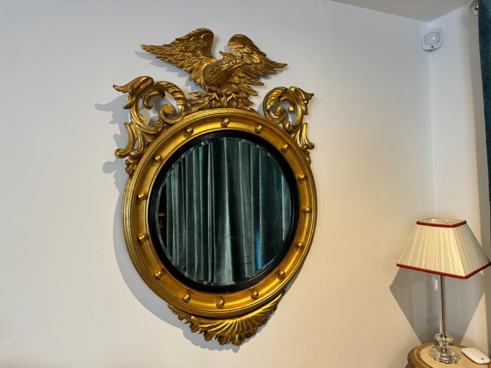 An oval Regency Revival giltwood wall mirror featuring a carved eagle cresting, ball embellishments, and an ebonised inner slip.