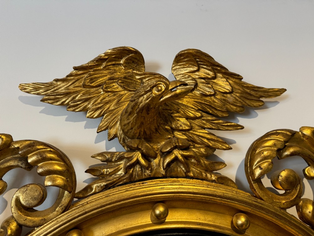 An oval Regency Revival giltwood wall mirror featuring a carved eagle cresting, ball embellishments, and an ebonised inner slip. View II