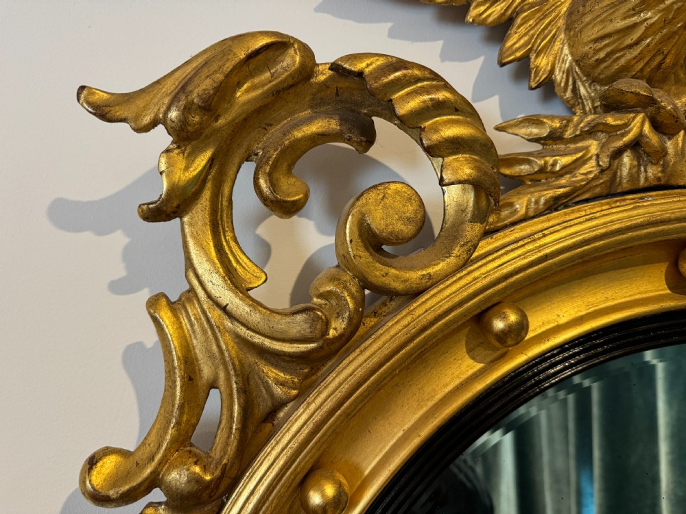 An oval Regency Revival giltwood wall mirror featuring a carved eagle cresting, ball embellishments, and an ebonised inner slip. View III