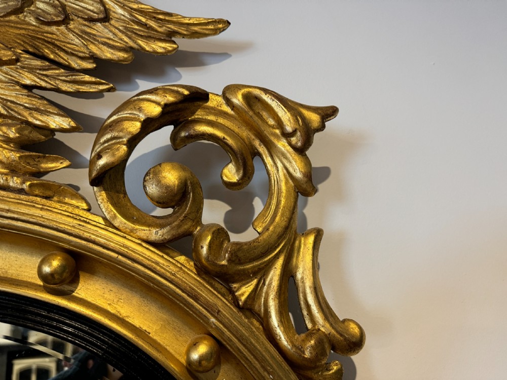 An oval Regency Revival giltwood wall mirror featuring a carved eagle cresting, ball embellishments, and an ebonised inner slip. View IV