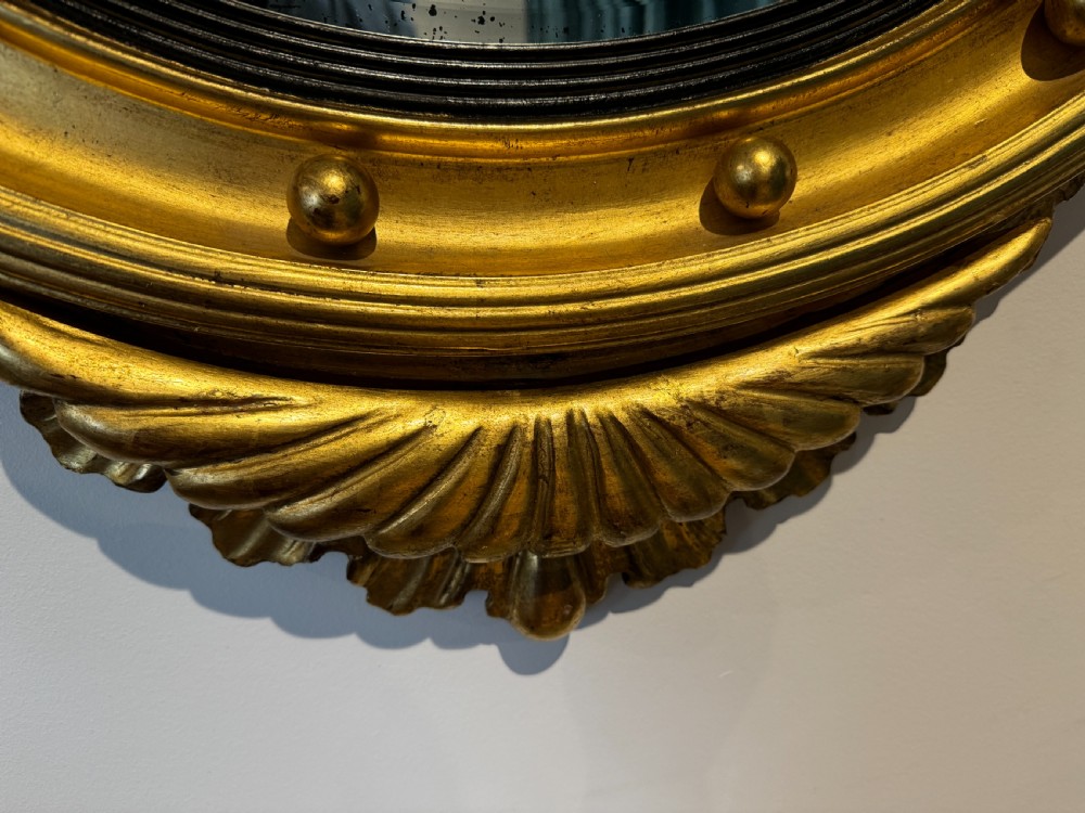 An oval Regency Revival giltwood wall mirror featuring a carved eagle cresting, ball embellishments, and an ebonised inner slip. View V