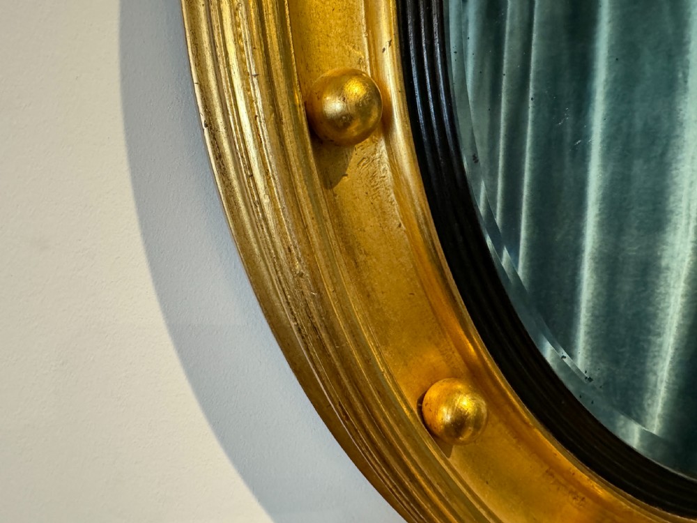 An oval Regency Revival giltwood wall mirror featuring a carved eagle cresting, ball embellishments, and an ebonised inner slip. View VI