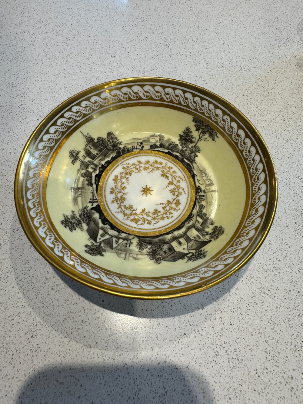 A straight-sided French porcelain coffee cup and saucer featuring hand-painted sepia landscape scenes, a pale yellow ground, and wide gold leaf borders. View III