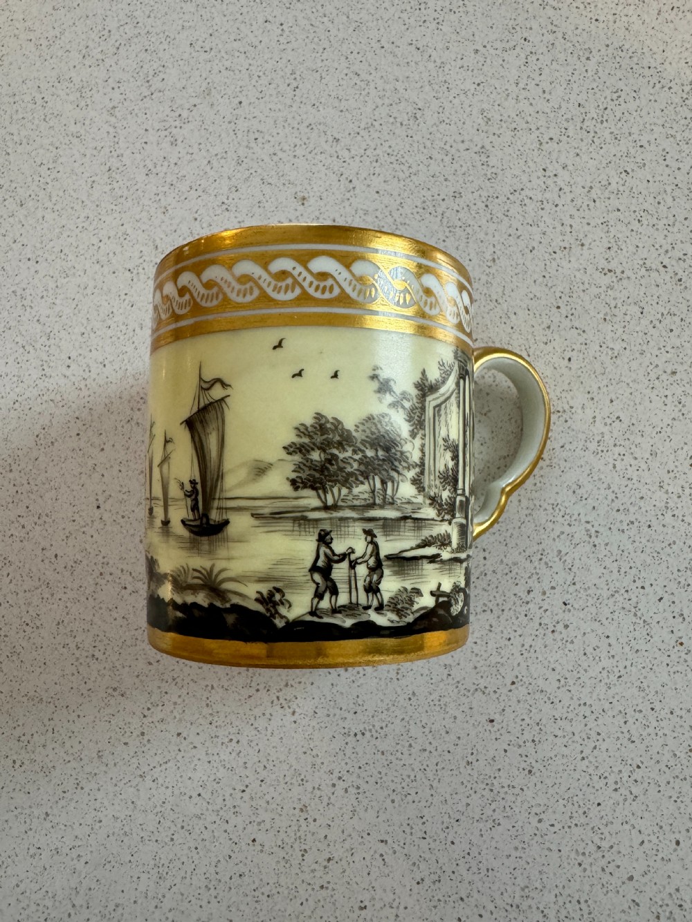 A straight-sided French porcelain coffee cup and saucer featuring hand-painted sepia landscape scenes, a pale yellow ground, and wide gold leaf borders. View IV