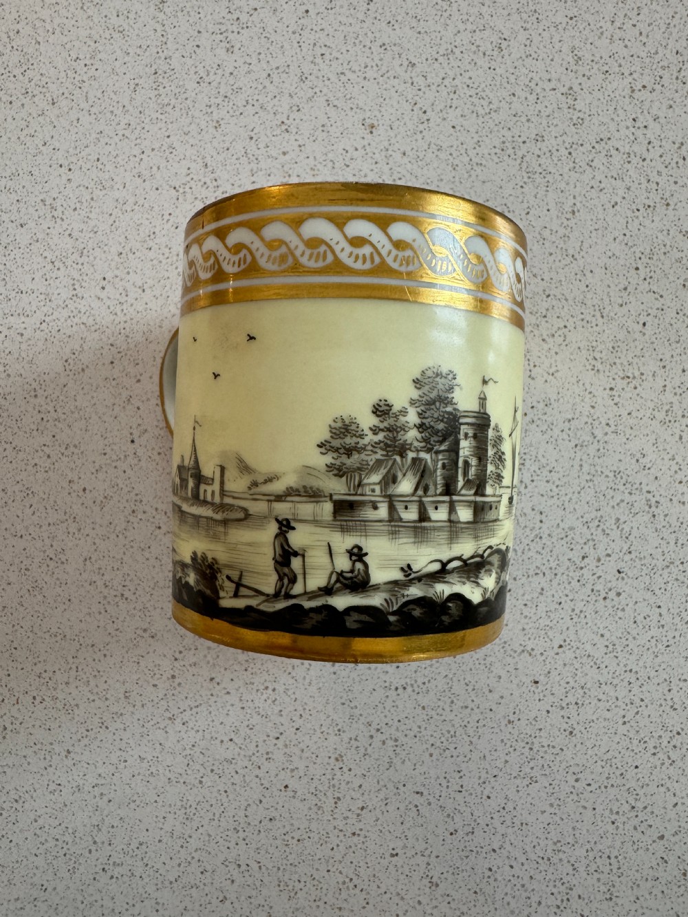 A straight-sided French porcelain coffee cup and saucer featuring hand-painted sepia landscape scenes, a pale yellow ground, and wide gold leaf borders. View V