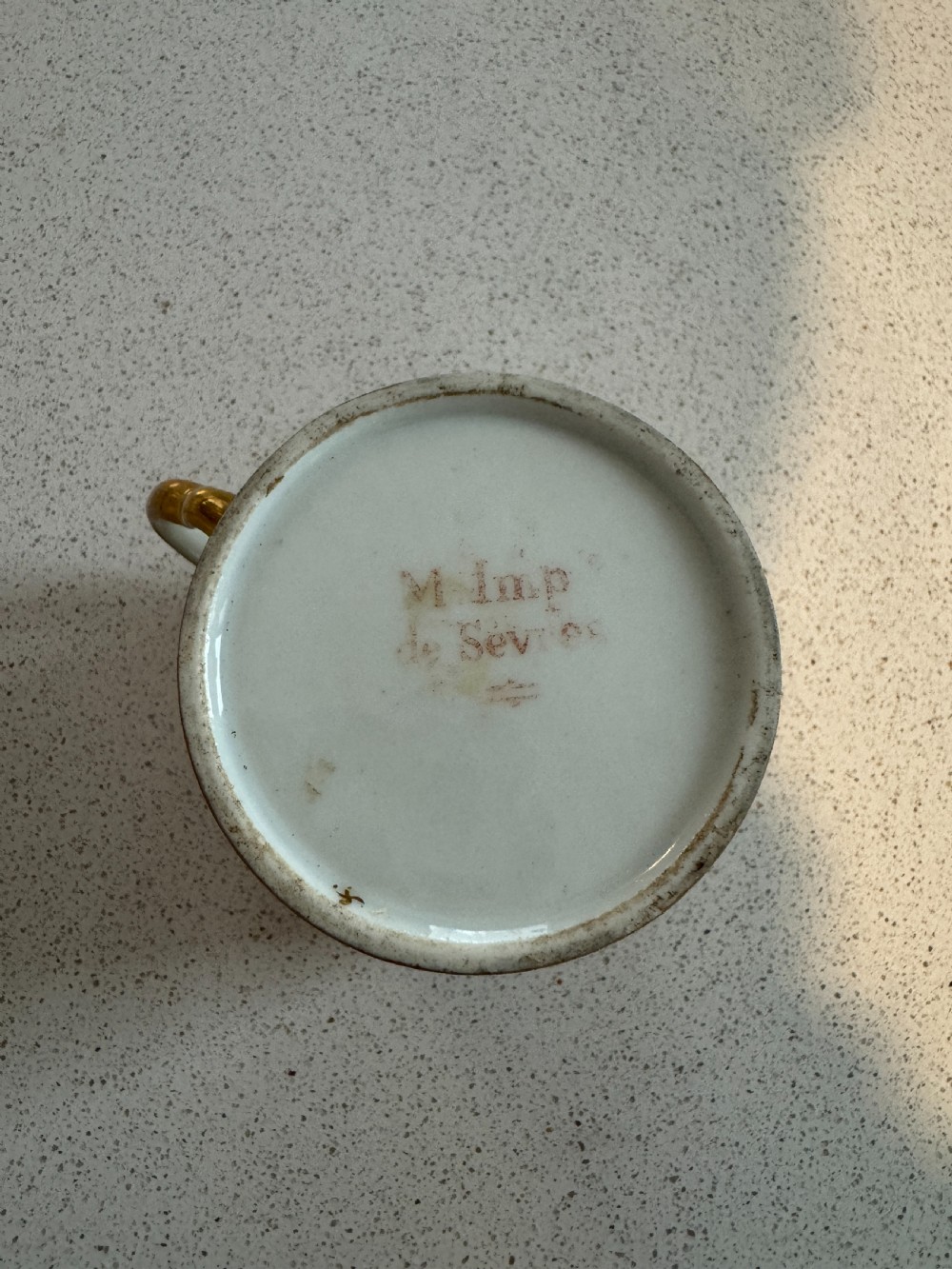 A straight-sided French porcelain coffee cup and saucer featuring hand-painted sepia landscape scenes, a pale yellow ground, and wide gold leaf borders. View VII