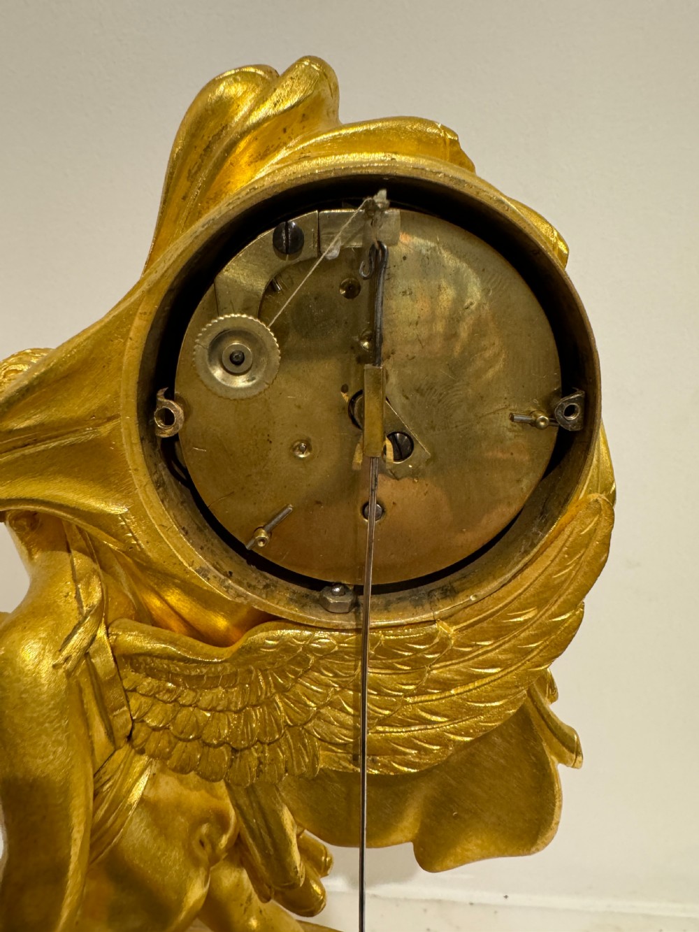 A French Empire gilt bronze table clock featuring a sculpted winged cherub figure supporting a circular white enamel dial set on an oval decorated base. View IV