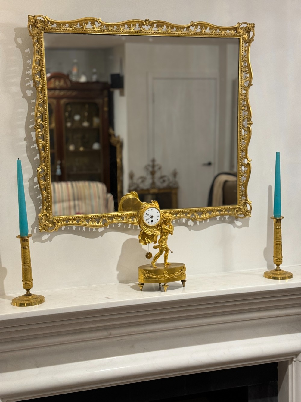 A French Empire gilt bronze table clock featuring a sculpted winged cherub figure supporting a circular white enamel dial set on an oval decorated base. View VIII