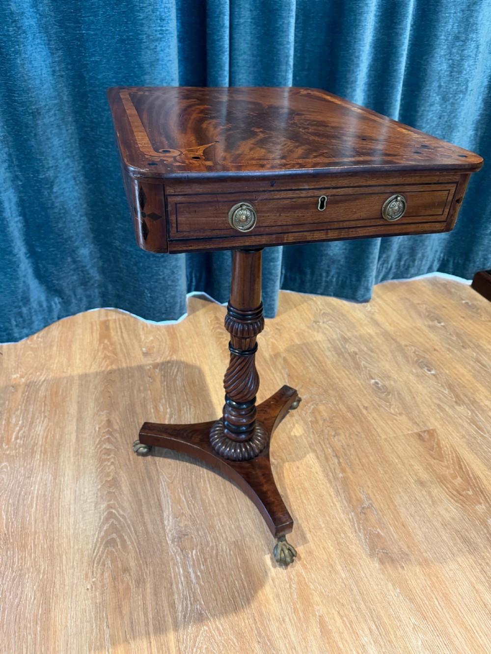 A Regency mahogany occasional table featuring a rectangular inlaid top above a single drawer, supported by a spiral-turned pedestal and a triform base on brass claw feet.