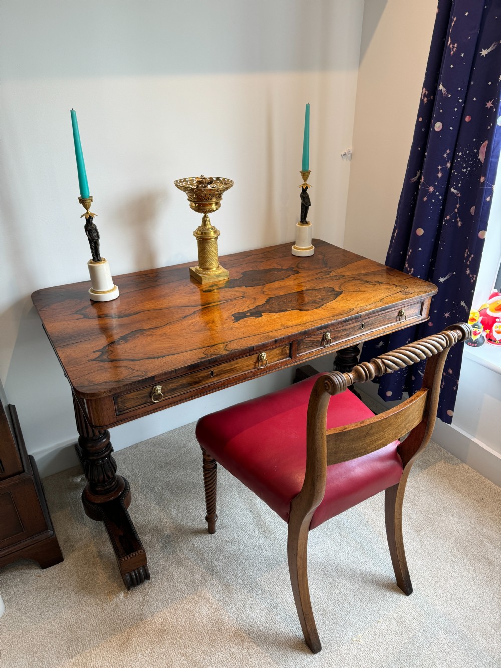 A Regency rosewood writing table featuring a highly figured top, two frieze drawers with brass lion-mask handles, and carved turned pedestal legs on trestle feet. View II