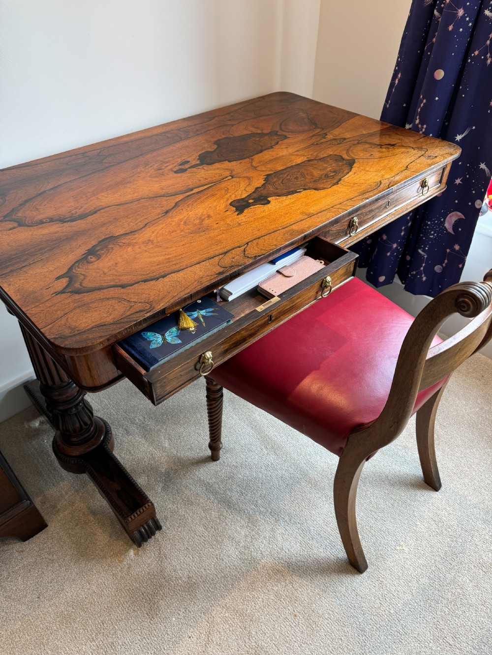 A Regency rosewood writing table featuring a highly figured top, two frieze drawers with brass lion-mask handles, and carved turned pedestal legs on trestle feet. View V