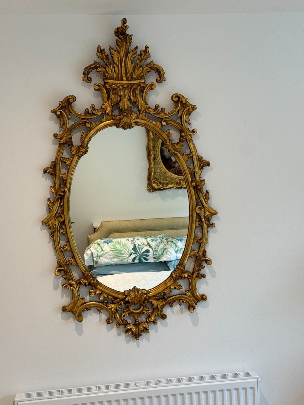 An ornate George III revival oval wall mirror featuring detailed carved giltwood scrollwork and an acanthus cresting.