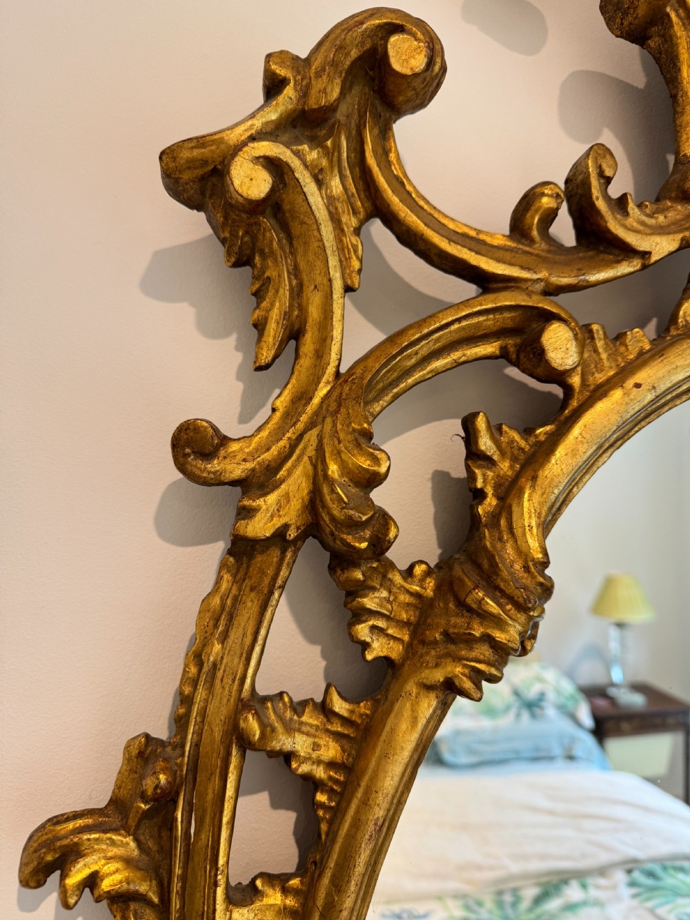 An ornate George III revival oval wall mirror featuring detailed carved giltwood scrollwork and an acanthus cresting. View III