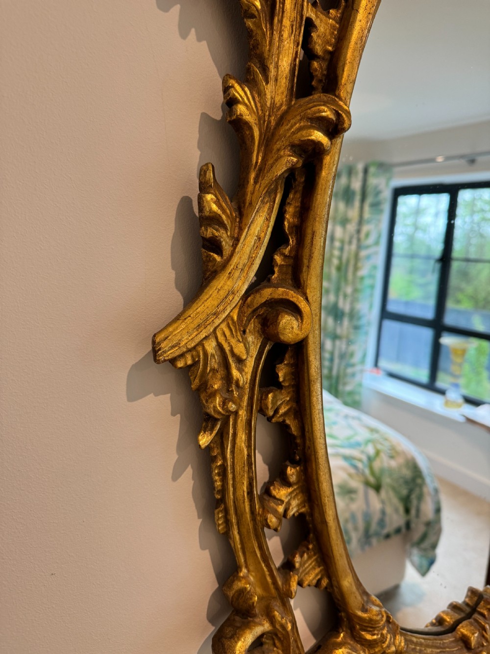 An ornate George III revival oval wall mirror featuring detailed carved giltwood scrollwork and an acanthus cresting. View V