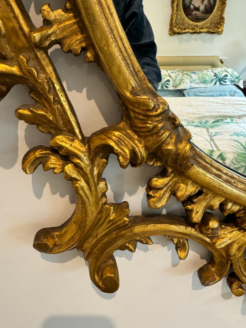 An ornate George III revival oval wall mirror featuring detailed carved giltwood scrollwork and an acanthus cresting. View VI
