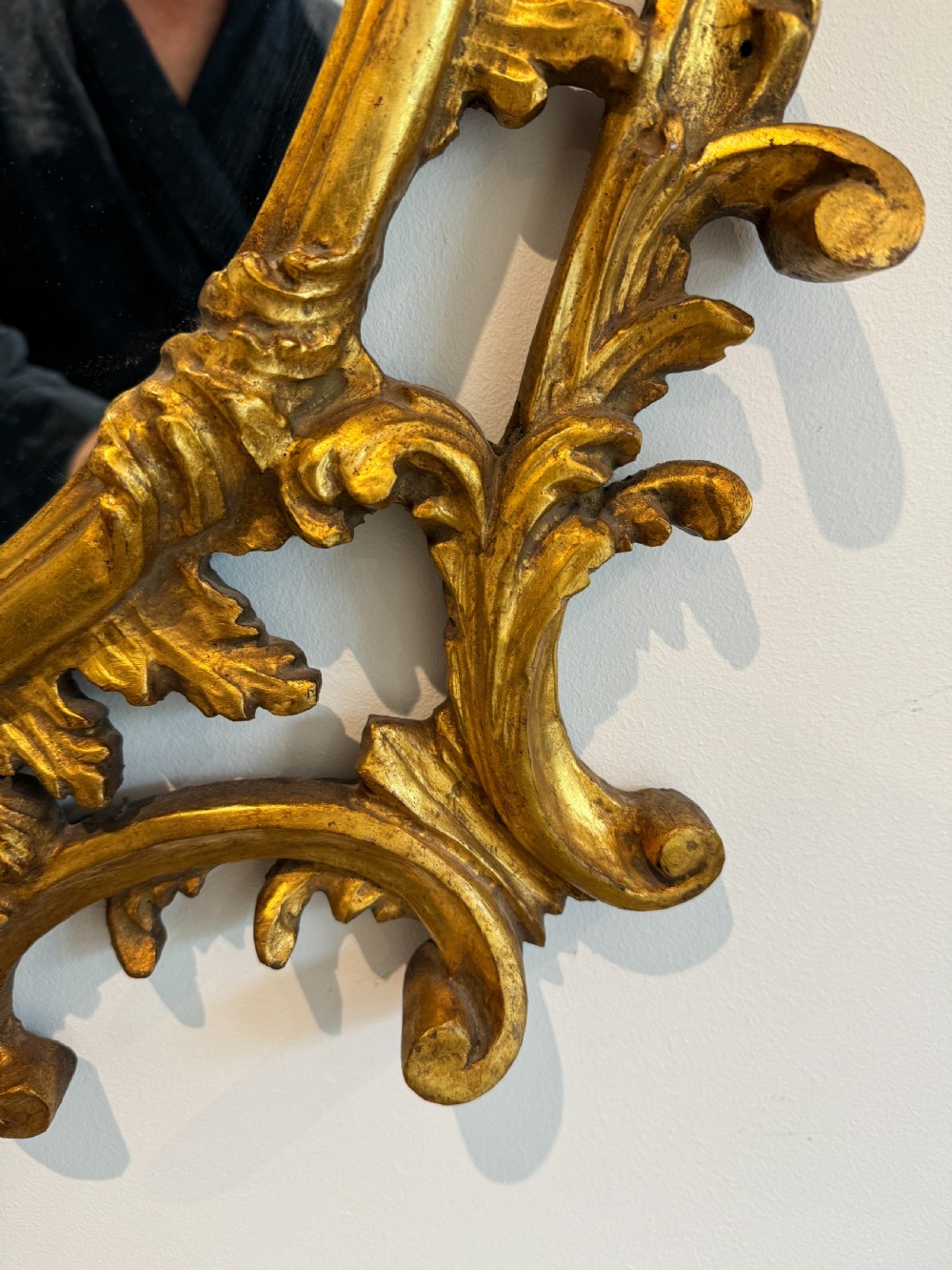An ornate George III revival oval wall mirror featuring detailed carved giltwood scrollwork and an acanthus cresting. View VII