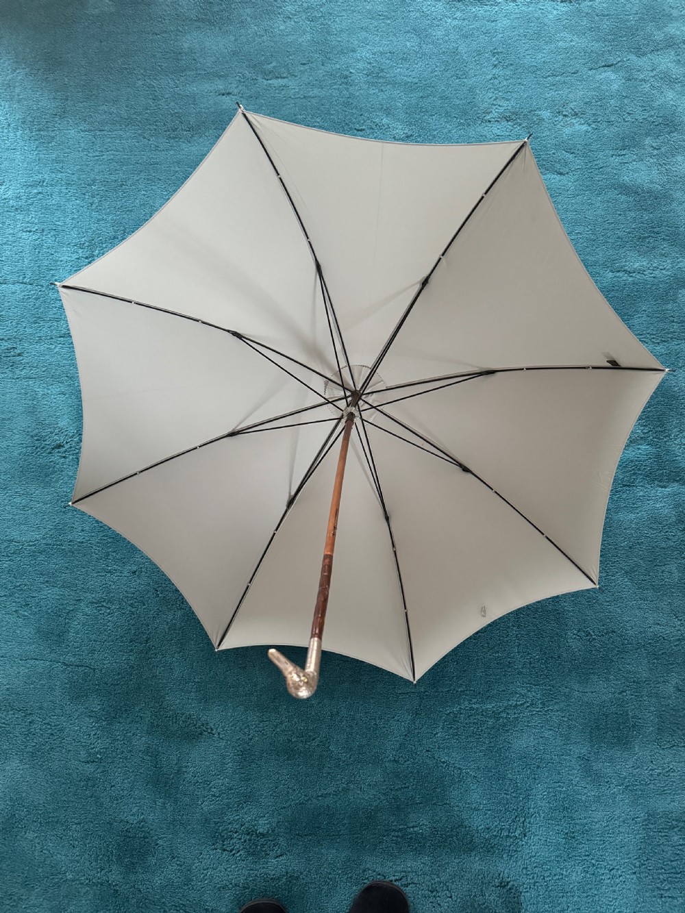 An Edwardian parasol featuring a carved silver duck head handle, a dark wooden shaft, and a folded sage green fabric canopy. View IV