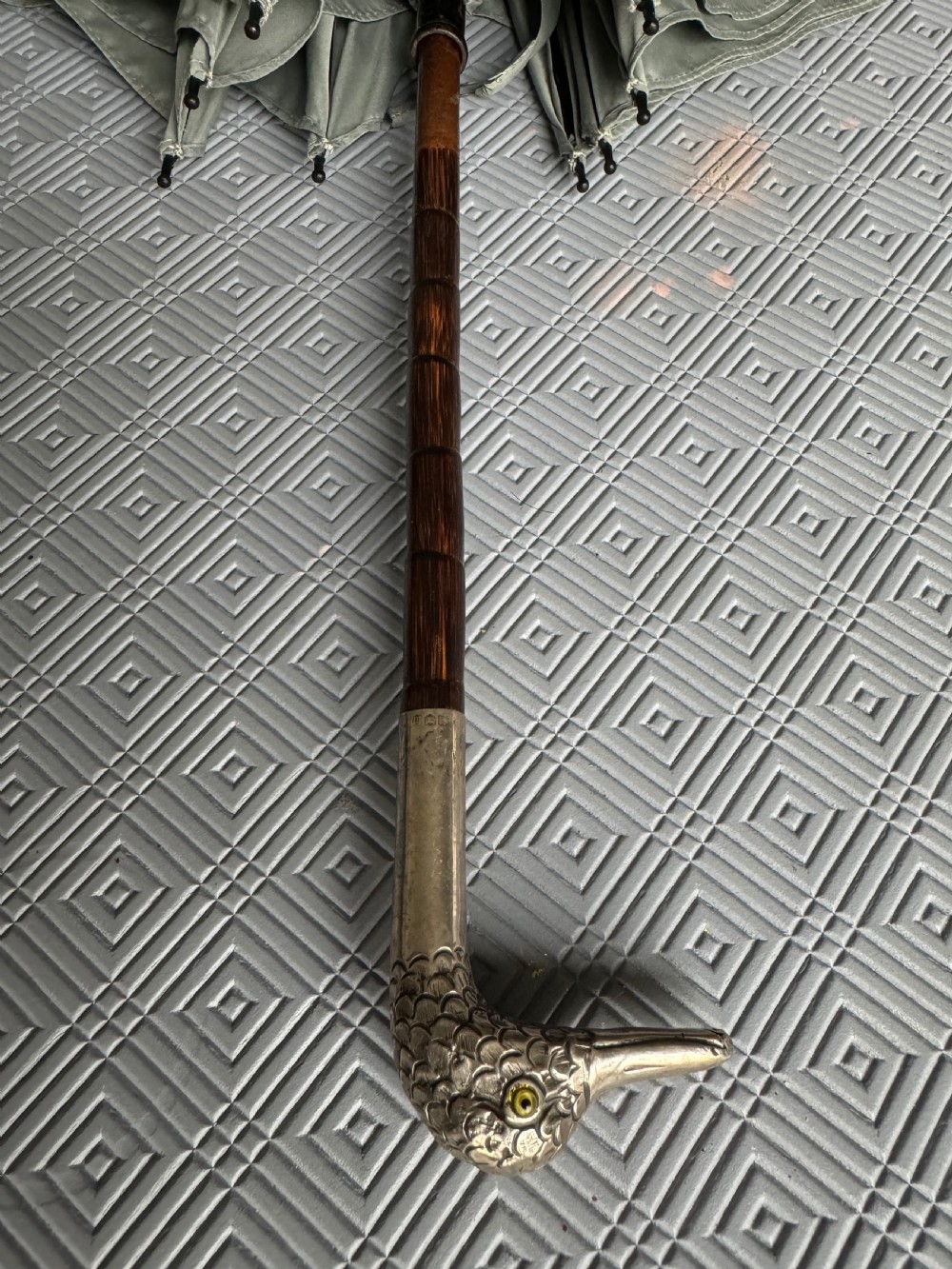 An Edwardian parasol featuring a carved silver duck head handle, a dark wooden shaft, and a folded sage green fabric canopy. View VII