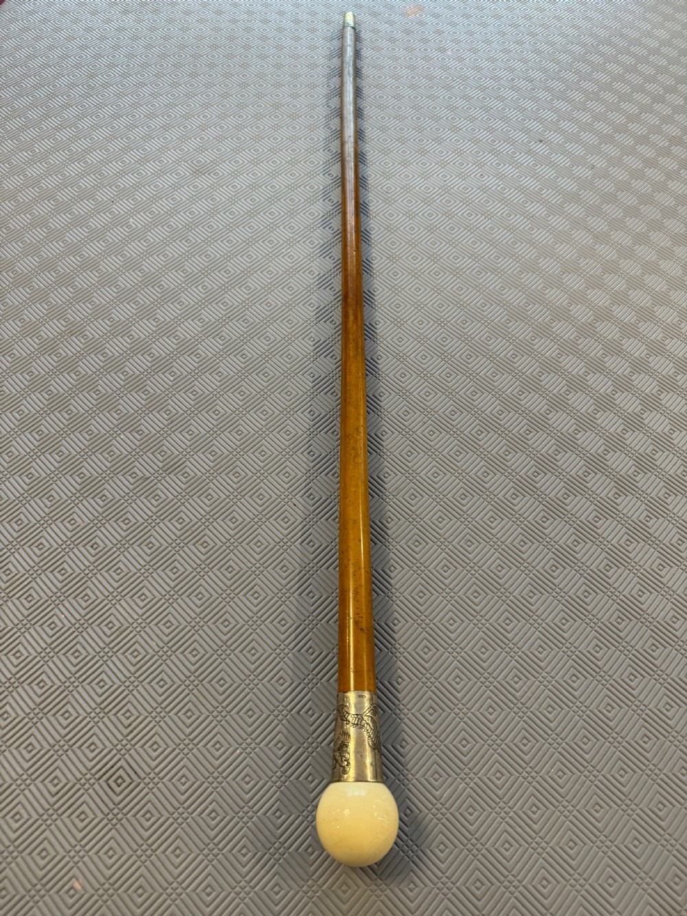 An antique wooden walking stick featuring a rounded cream pommel and an embossed silver collar decorated with a dragon motif.