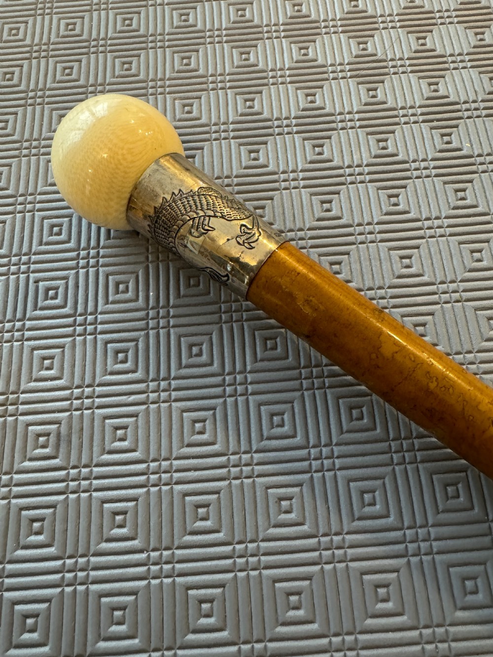 An antique wooden walking stick featuring a rounded cream pommel and an embossed silver collar decorated with a dragon motif. View II