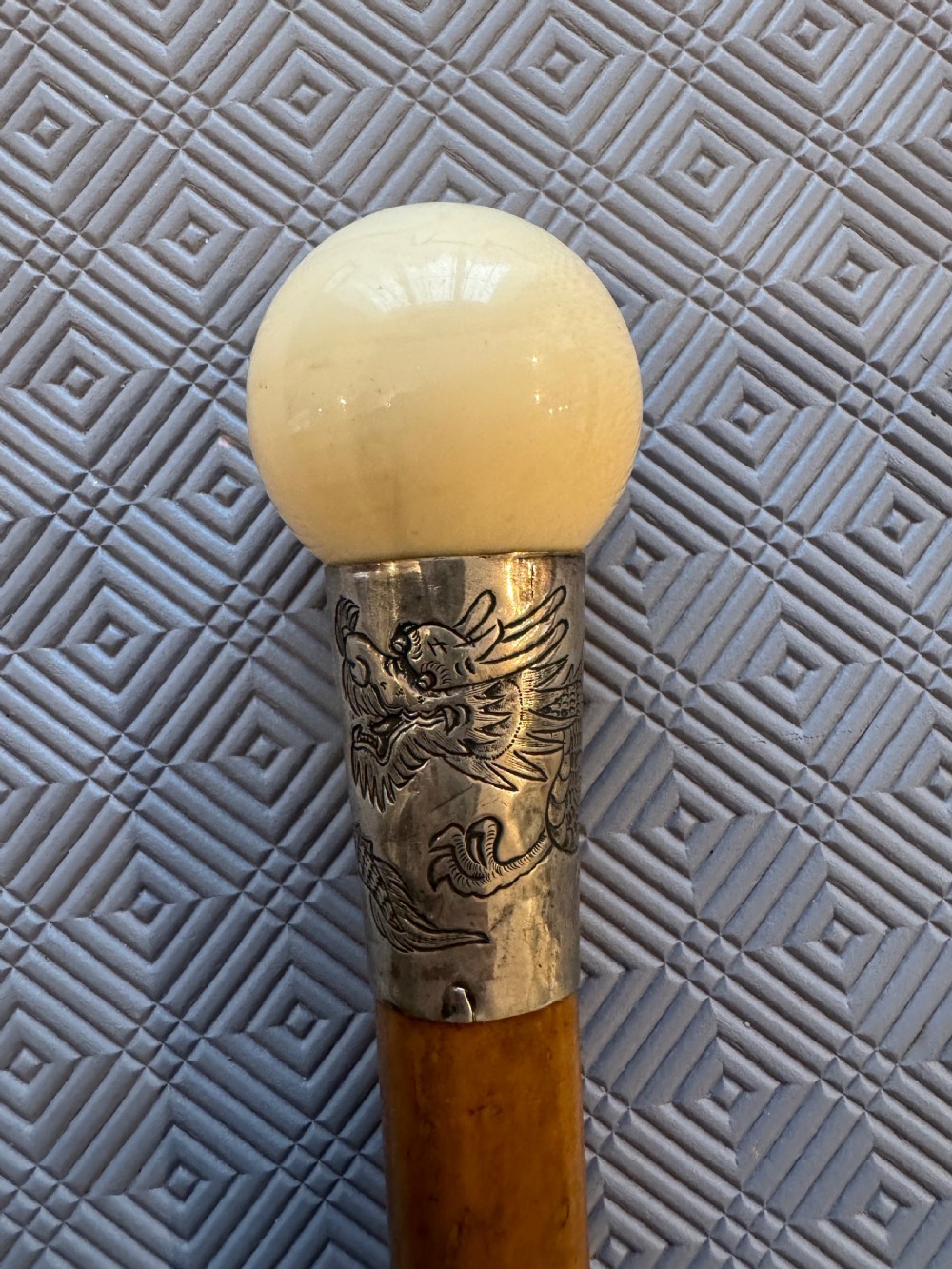 An antique wooden walking stick featuring a rounded cream pommel and an embossed silver collar decorated with a dragon motif. View III