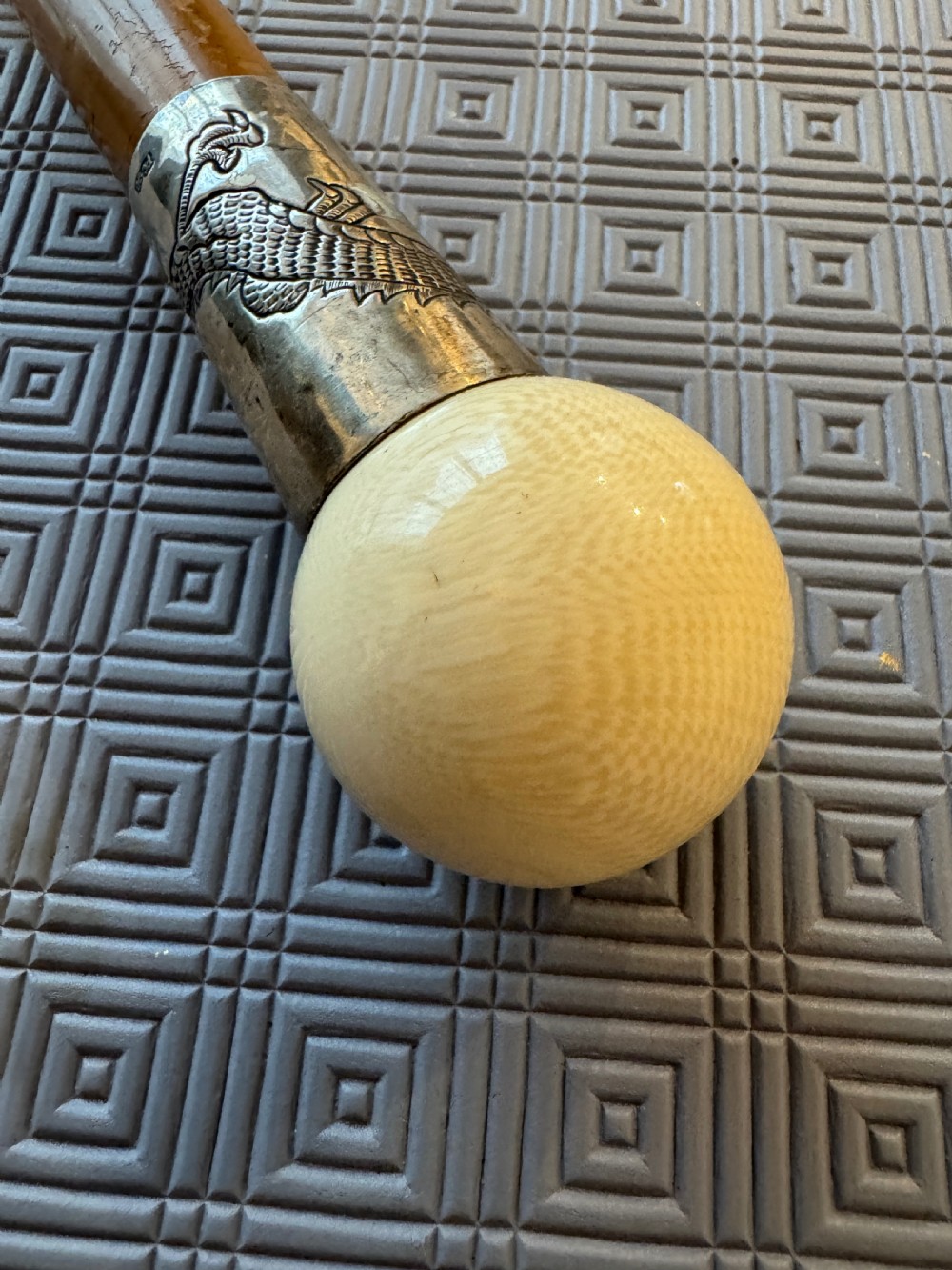 An antique wooden walking stick featuring a rounded cream pommel and an embossed silver collar decorated with a dragon motif. View IV