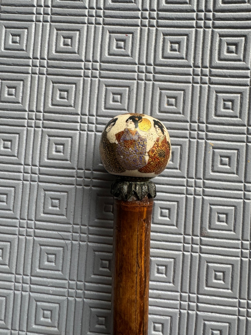 A dark brown bamboo walking stick featuring a cream and gold painted ceramic pommel handle. View II