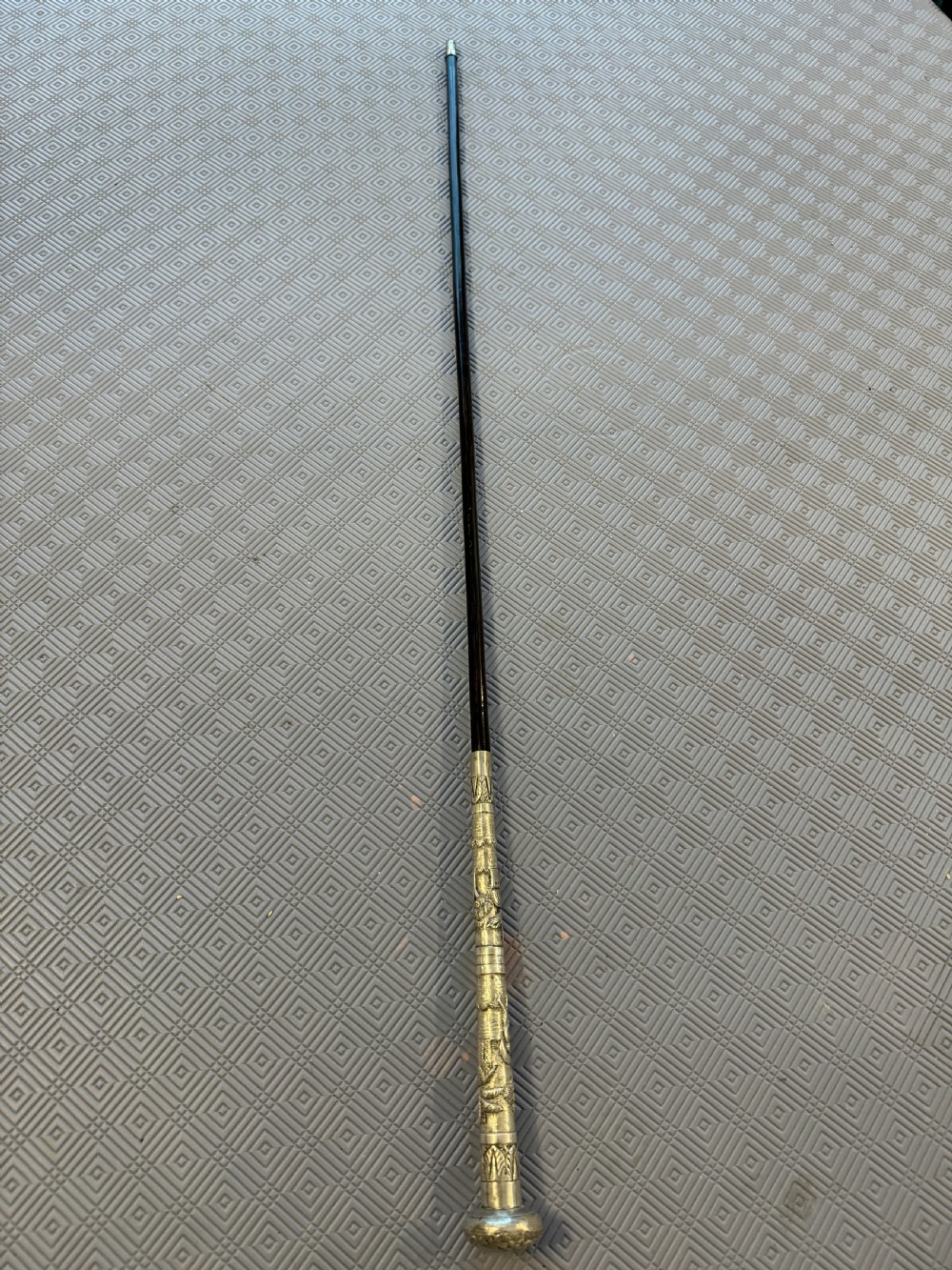 An antique Chinese sword stick featuring a dark wood shaft and an intricately detailed, silver-coloured metal handle decorated with raised figural motifs.