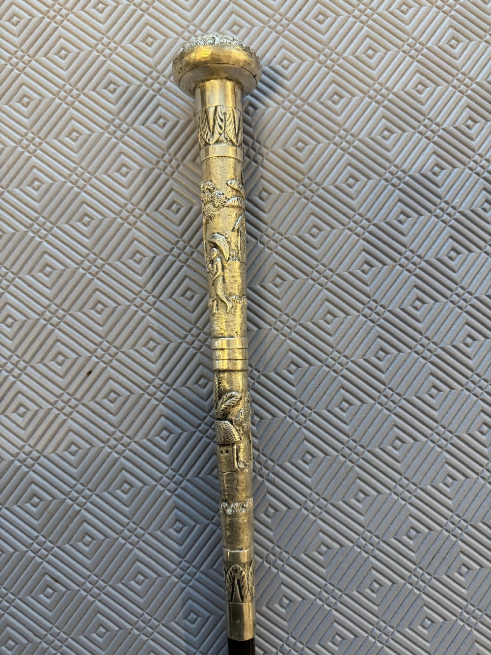 An antique Chinese sword stick featuring a dark wood shaft and an intricately detailed, silver-coloured metal handle decorated with raised figural motifs. View II