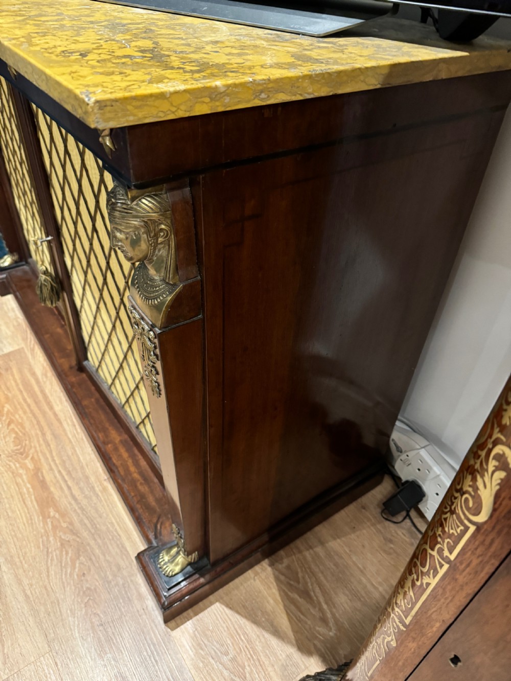 A Regency period dark mahogany side cabinet featuring an original yellow breche marble top, Egyptian revival gilt bronze mounts, and brass wire grille doors with pleated silk backing. View III