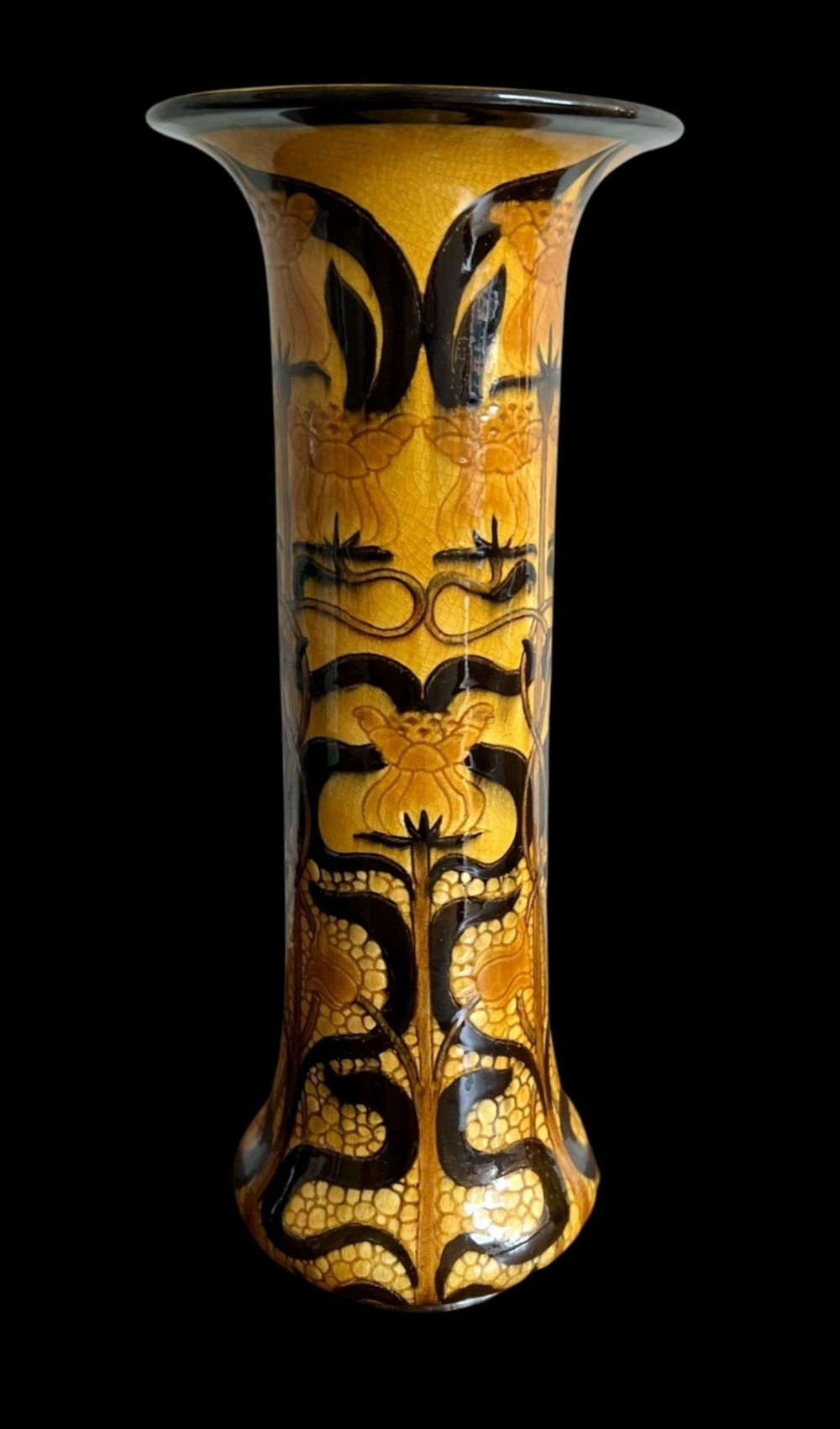 A tall cylindrical Art Nouveau glazed earthenware vase featuring dark brown stylised floral motifs over a warm yellow crackle glaze base.