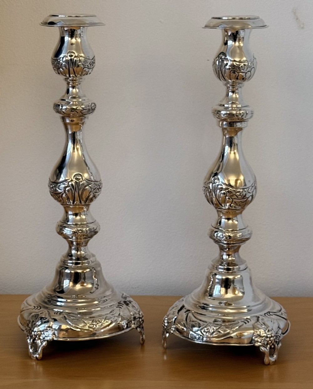 A pair of tall, polished sterling silver Shabbat candlesticks featuring ornate knopped stems and repousse foliate bases.