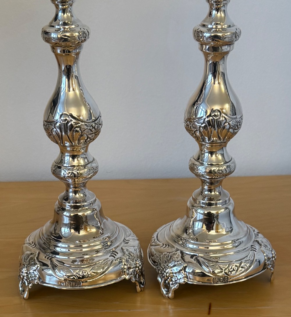 A pair of tall, polished sterling silver Shabbat candlesticks featuring ornate knopped stems and repousse foliate bases. View V